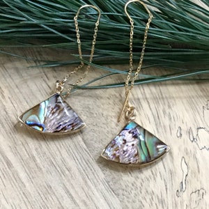 Può includere: Un paio di orecchini dorati con pendenti a forma di ventaglio in madreperla di abalone iridescente appesi a delicate catene.