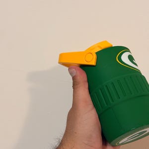 Puede incluir: Vaso t&eacute;rmico verde y amarillo con el logotipo de los Green Bay Packers. El vaso tiene una tapa abatible amarilla y un cuerpo verde con estr&iacute;as verticales. El logotipo de los Packers es una 'G' blanca sobre fondo verde.