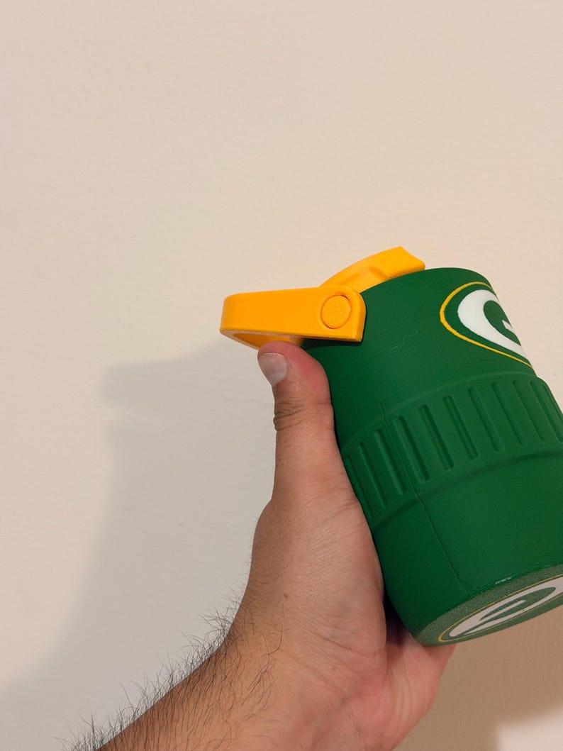 Puede incluir: Vaso t&eacute;rmico verde y amarillo con el logotipo de los Green Bay Packers. El vaso tiene una tapa abatible amarilla y un cuerpo verde con estr&iacute;as verticales. El logotipo de los Packers es una 'G' blanca sobre fondo verde.