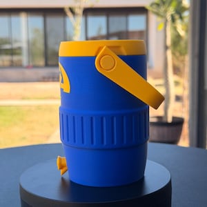 May include: A blue and yellow water cooler with a yellow handle and lid. The cooler has a spigot and a logo on the side. The cooler is sitting on a black surface.