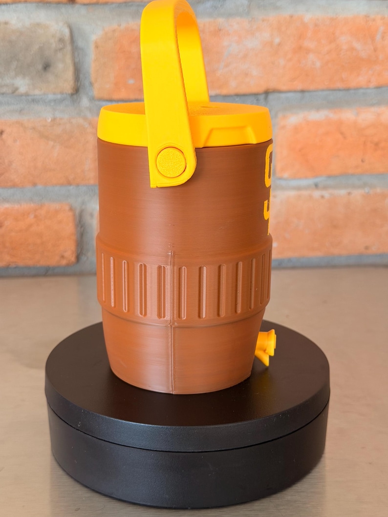 May include: A brown and yellow water cooler with a handle. The cooler has a cylindrical shape with a yellow handle and lid. The cooler has a spigot and a ribbed design around the base. The number "9" is visible on the side.