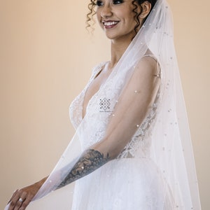 A single-layer oval shape veil made from a lightweight, ultra soft tulle covered in pearl stud beads. Shown in Light Ivory.