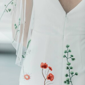 May include: White dress with a zipper closure and floral embroidery. The embroidery features green leaves and red flowers.