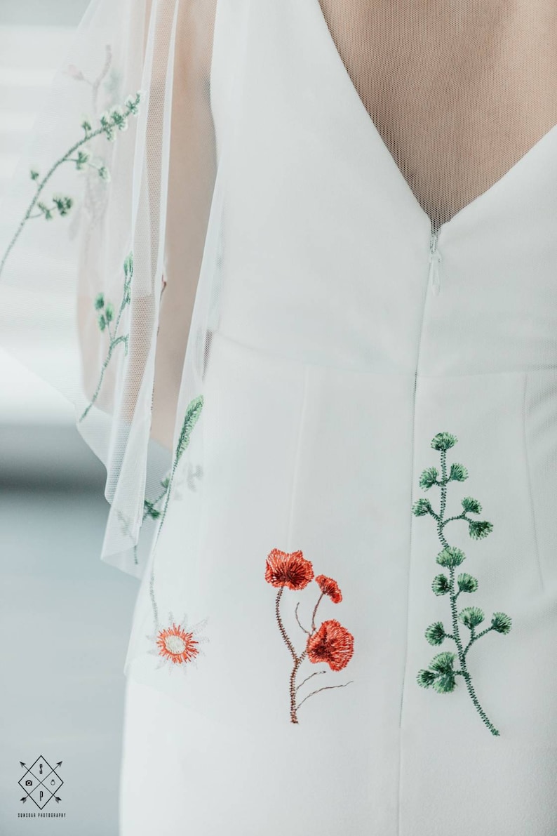 May include: White dress with a zipper closure and floral embroidery. The embroidery features green leaves and red flowers.