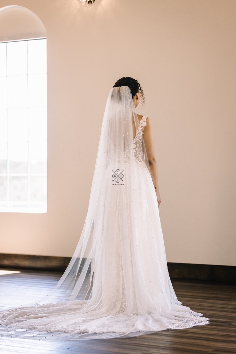A single-layer oval shape veil made from a lightweight, ultra soft tulle covered in pearl stud beads. Shown in Light Ivory.