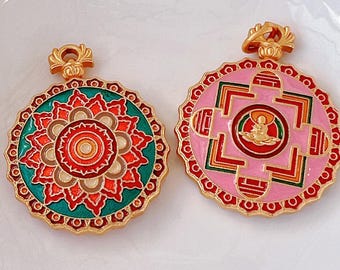 Puede incluir: Dos colgantes dorados con diseños intrincados. Uno es turquesa y naranja, el otro rosa y rojo, ambos con una figura central. Los colgantes tienen forma circular con patrones detallados y un lazo superior decorativo.