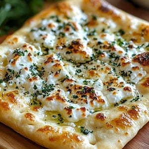 May include: A rectangular flatbread topped with white cheese and green herbs, drizzled with oil. The bread has a golden-brown crust and is served on a wooden surface. A close-up shot highlights the textures and ingredients.