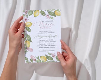 May include: A bridal shower invitation with a watercolor lemon and floral design. The invitation reads "She Found Her Main Squeeze" and includes event details. The invitation is held against a white background.