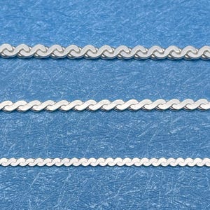 May include: Three silver-colored chain necklaces with a wavy, textured design are displayed against a blue background. The chains vary in thickness, with the top chain being the thickest and the bottom chain the thinnest.