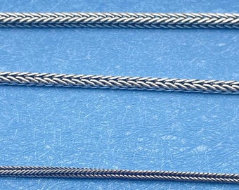 May include: Three silver-colored chain necklaces with a woven design are displayed against a blue background. The chains vary in thickness, showcasing different styles of jewelry.