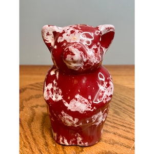 May include: A ceramic bear figurine in a glossy red finish with white splatter details. The bear has a rounded body, small ears, and a detailed face. The figurine is a decorative item.