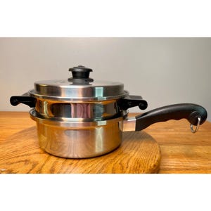 May include: A stainless steel double boiler pot featuring a polished finish, a matching lid with a black knob, and a long black handle with a metal hanging loop. The upper insert rests securely within the base pot, both constructed from durable metal.