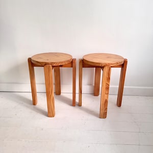 May include: Two wooden stools with round seats and angled legs. The stools are made of light-coloured wood and have a simple, minimalist design. The seats are approximately 30 cm in diameter.