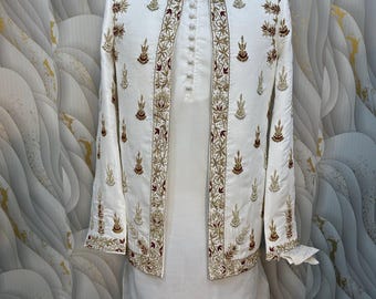May include: A white embroidered jacket and tunic set. The jacket has detailed gold and burgundy embroidery on the borders and sleeves. The tunic has a mandarin collar and a button-down front. The outfit is displayed on a mannequin.