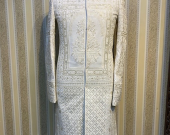 Könnte beinhalten: Elfenbeinfarbene, langärmlige formelle Jacke mit aufwendiger goldener Stickerei. Die Jacke hat einen Stehkragen und einen vertikalen Reißverschluss. Das Design umfasst detaillierte Muster auf den Vorderteilen, Ärmeln und dem unteren Bereich.