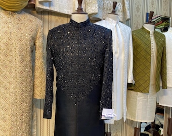 Peut inclure: Une tunique noire brodée avec un col mandarin, présentée sur un mannequin. La tunique présente des broderies complexes sur la partie supérieure et des manches longues. D'autres vêtements de différentes couleurs et motifs sont visibles en arrière-plan.