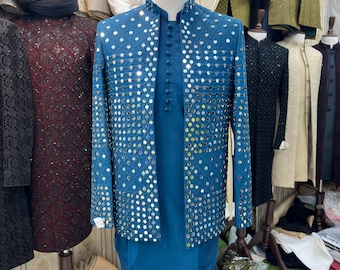 May include: A teal formal suit featuring a jacket embellished with reflective details. The jacket is worn with a matching tunic and trousers. Other formal attire, including jackets and turbans, are visible in the background.