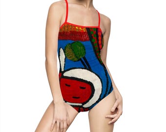 May include: A one-piece swimsuit with a colorful, abstract design. The swimsuit features a red trim and straps, with a blue background and a whimsical face design. The artwork includes red, green, and orange elements.