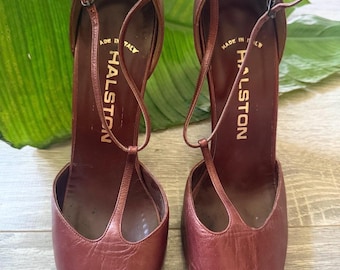 May include: A pair of dark brown leather peep-toe high heels with T-strap closures and thin ankle straps. The interior footbeds are stamped with the gold text HALSTON and MADE IN ITALY. The shoes feature a textured leather finish.