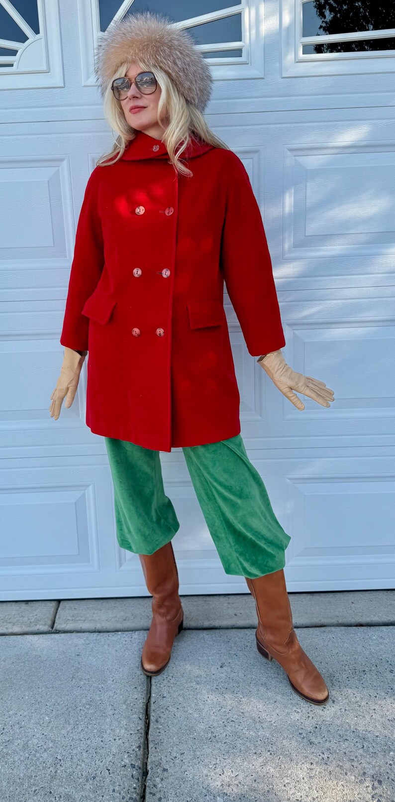 K&ouml;nnte beinhalten: Ein roter, zweireihiger Mantel mit gro&szlig;en Kn&ouml;pfen, kombiniert mit einer gr&uuml;nen Samthose und braunen Stiefeln. Das Outfit wird durch einen Pelzhut und Handschuhe erg&auml;nzt. Der Mantel hat zwei Vordertaschen.