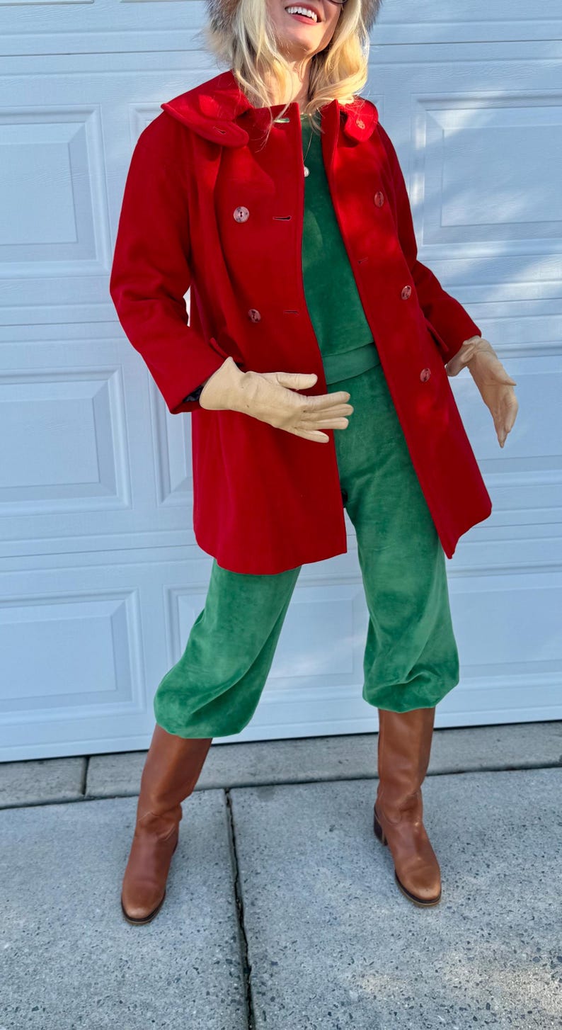 K&ouml;nnte beinhalten: Eine Person tr&auml;gt einen roten, zweireihigen Mantel, eine gr&uuml;ne Samthose und braune Lederstiefel. Das Outfit umfasst ein gr&uuml;nes Oberteil und beige Handschuhe. Ein Pelzhut vervollst&auml;ndigt den Look.