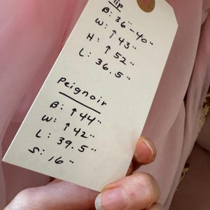 May include: A pink slip and peignoir with measurements listed on a tag. The slip measurements are: bust 36-40 inches, waist 43 inches, height 52 inches, and length 36.5 inches. The peignoir measurements are: bust 44 inches, waist 42 inches, length 39.5 inches, and sleeve 16 inches.