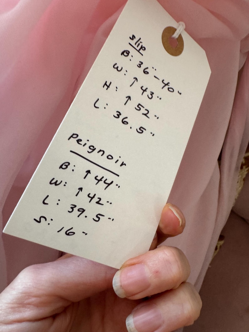 May include: A pink slip and peignoir with measurements listed on a tag. The slip measurements are: bust 36-40 inches, waist 43 inches, height 52 inches, and length 36.5 inches. The peignoir measurements are: bust 44 inches, waist 42 inches, length 39.5 inches, and sleeve 16 inches.