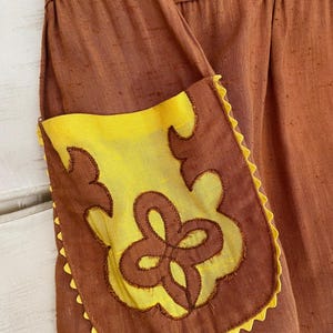 May include: A brown skirt with a yellow pocket. The pocket has a brown embroidered design.