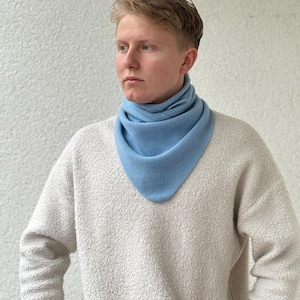Peut inclure: Un tour de cou bleu clair est porté autour du cou. Le tour de cou est fait d'une matière douce. La personne porte un pull crème. L'arrière-plan est un mur blanc.