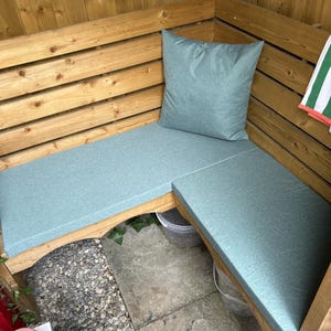 May include: A wooden outdoor bench with light blue cushions and a matching pillow. The bench is built into a wooden structure, creating a cozy seating area. A green and white striped towel hangs nearby.