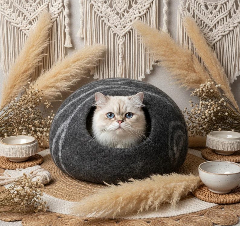 May include: A gray cat bed with a white and gray striped design, housing a fluffy white cat with blue eyes. The cat bed is surrounded by decorative elements, including dried plants and small ceramic bowls, creating a cozy and stylish pet accessory.