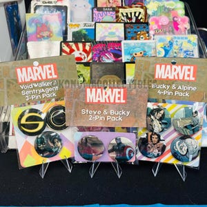 May include: Marvel-themed pin packs featuring characters like Steve, Bucky, and others. The packs include 2, 3, and 4-pin sets with colorful graphics. The Marvel logo is prominently displayed on the packaging, with the names of the characters.