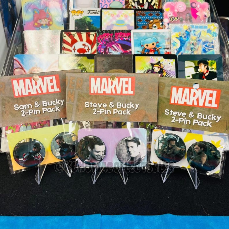 May include: Marvel 2-pin packs featuring Sam & Bucky and Steve & Bucky. Each pack includes two round pins with character images. The Marvel logo is displayed on the packaging. The background includes various collectible cards.