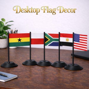 Może przedstawiać: Zestaw flag na biurko, w tym Ghana, Polska, RPA, Egipt i Stany Zjednoczone. Każda flaga jest zamontowana na czarnym stojaku. Flagi są prezentowane na drewnianej powierzchni, z napisem "Desktop Flag Decor" w złotym kolorze.
