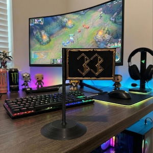 May include: A black desk flag with the number "33" in gold, set against a gaming setup. The flag is rectangular with a gold border and a black background. The base is round. A curved monitor and keyboard are in the background.