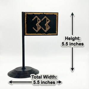 May include: A black and gold flag-shaped decoration with the number "33" in a stylized font. The flag is 5.5 inches in height and 5.5 inches wide, mounted on a black stand.