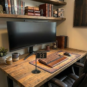 May include: A rustic wooden desk with a computer monitor, keyboard, and mouse. The desk features a leather mousepad, a small flag, and two mugs. Bookshelves with books and figurines are above the desk.