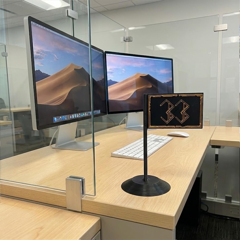 May include: A black desk flag with the number "33" in gold lettering. The flag is on a black stand, and sits on a light wood desk. Two computer monitors are in the background.