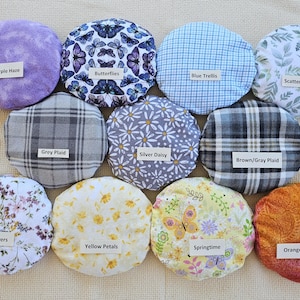 May include: A collection of eleven round fabric items with various patterns and colors. Designs include butterflies, floral, plaid, and abstract patterns. Each item has a small label with a descriptive name such as "Purple Haze" or "Springtime".