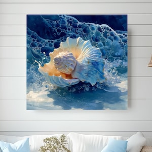 May include: A square canvas print depicts a seashell in shades of blue and cream, emerging from foamy water. The artwork hangs above a white sofa with blue pillows, a wooden coffee table, and a woven ottoman, creating a coastal theme.