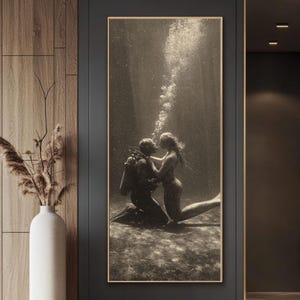 Könnte beinhalten: Sepiafarbener Kunstdruck mit Rahmen, der einen Taucher und eine Meerjungfrau unter Wasser zeigt. Der Taucher kniet und blickt die Meerjungfrau an, die sich ausstreckt. Blasen steigen vom Taucher auf. Das Kunstwerk wird an einer dunkelgrauen Wand ausgestellt.