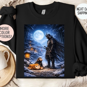 May include: Black sweatshirt featuring a detailed illustration of a samurai warrior standing in a snowy landscape under a full moon. Two monkeys are in the foreground. The image includes a Japanese temple and forest. The text "MORE COLOR OPTIONS!" is on the left.