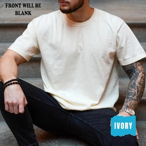 May include: Ivory-coloured short-sleeved t-shirt. The text "FRONT WILL BE BLANK" is at the top. The word "IVORY" is in a blue box at the bottom. The shirt is being worn by a person wearing black jeans and a black bracelet.