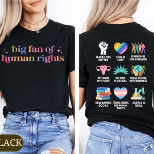 May include: Black t-shirt with the text "big fan of human rights" in colorful letters. The back of the shirt features various graphics and phrases, including "Black Lives Matter" and "Love is Love."