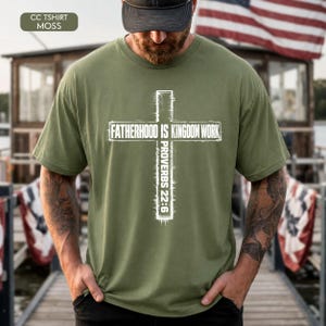 May include: Moss green t-shirt with a white cross design. The cross contains the text "FATHERHOOD IS KINGDOM WORK" and "PROVERBS 22:6". The shirt is a crew neck and has short sleeves.