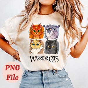 May include: Cream-colored t-shirt featuring four cartoon cat portraits in orange, gray, yellow, and black. The text "WARRIOR CATS" is printed in black below the cat illustrations. The shirt is made of a soft material.