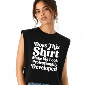 May include: A black sleeveless crop top featuring white text that reads Does This Shirt Make Me Look Professionally Developed in a bold, retro-inspired font. The garment has a crew neckline and wide shoulder openings, providing a relaxed fit.
