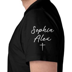 May include: Black short-sleeved shirt with the names "Sophia" and "Alex" in white script, along with a white cross. The shirt is made of a soft material.