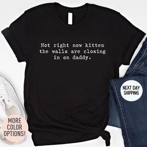 May include: Black t-shirt with the text "Not right now kitten the walls are closing in on daddy." The shirt is paired with blue jeans and white sneakers. Additional text on the image says "MORE COLOR OPTIONS!" and "NEXT DAY SHIPPING".