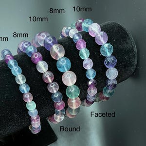 May include: Four bracelets with colorful fluorite beads. The bracelets feature round and faceted beads in various sizes: 6mm, 8mm, and 10mm. The beads are in shades of blue, purple, pink, and green.
